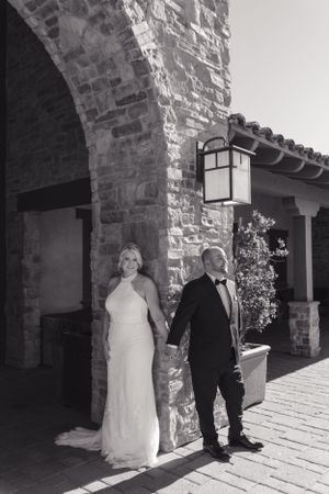 A black and white wedding photo of a couple posing against a stone wall with Spanish-style architecture and lantern.