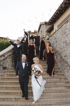 Wedding party descends outdoor stone staircase with bridal party members wearing burgundy dresses and dark suits.