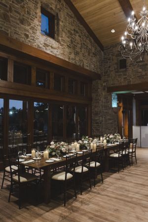 Elegant rustic reception venue with stone walls, chandelier, and long wooden tables set for a wedding dinner.