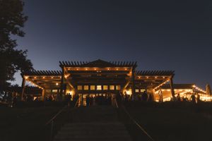 Illuminated rustic wedding venue at dusk with wooden pergola and warm lighting creating romantic ambiance.