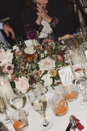Close-up of wedding reception table settings with pink and purple floral arrangements and wine glasses.