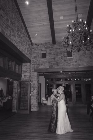 A couple shares a dance moment in an elegant stone-walled venue with a grand chandelier overhead.