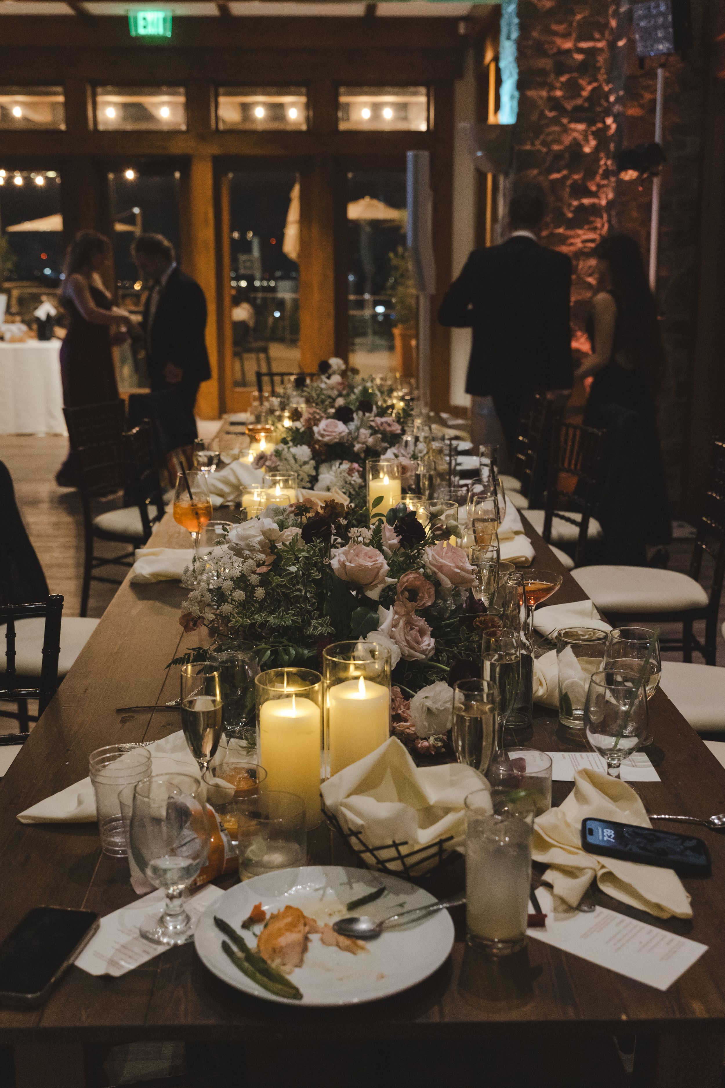 Elegant wedding reception table with moody lighting, lit candles, and rustic floral centerpieces at a formal dinner venue.