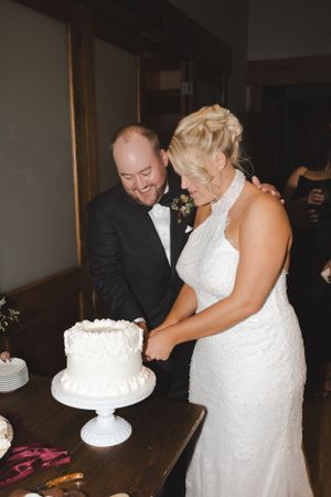 Couple sharing a laugh while cutting their white wedding cake at reception.