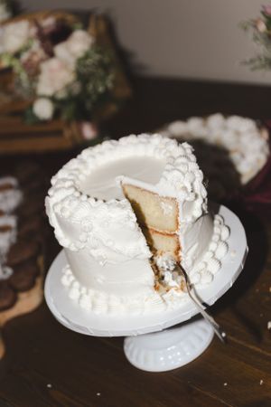 Classic white wedding cake with piped details and pearl decorations being served on a cake stand.