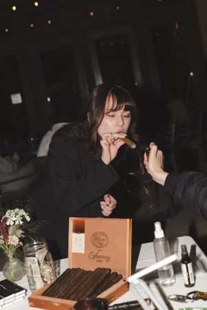 Guest examining cigar from wooden box at dimly lit reception table.