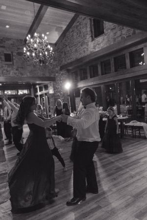 Couples dance together on a hardwood floor beneath a chandelier in a rustic stone-walled venue during an elegant event.