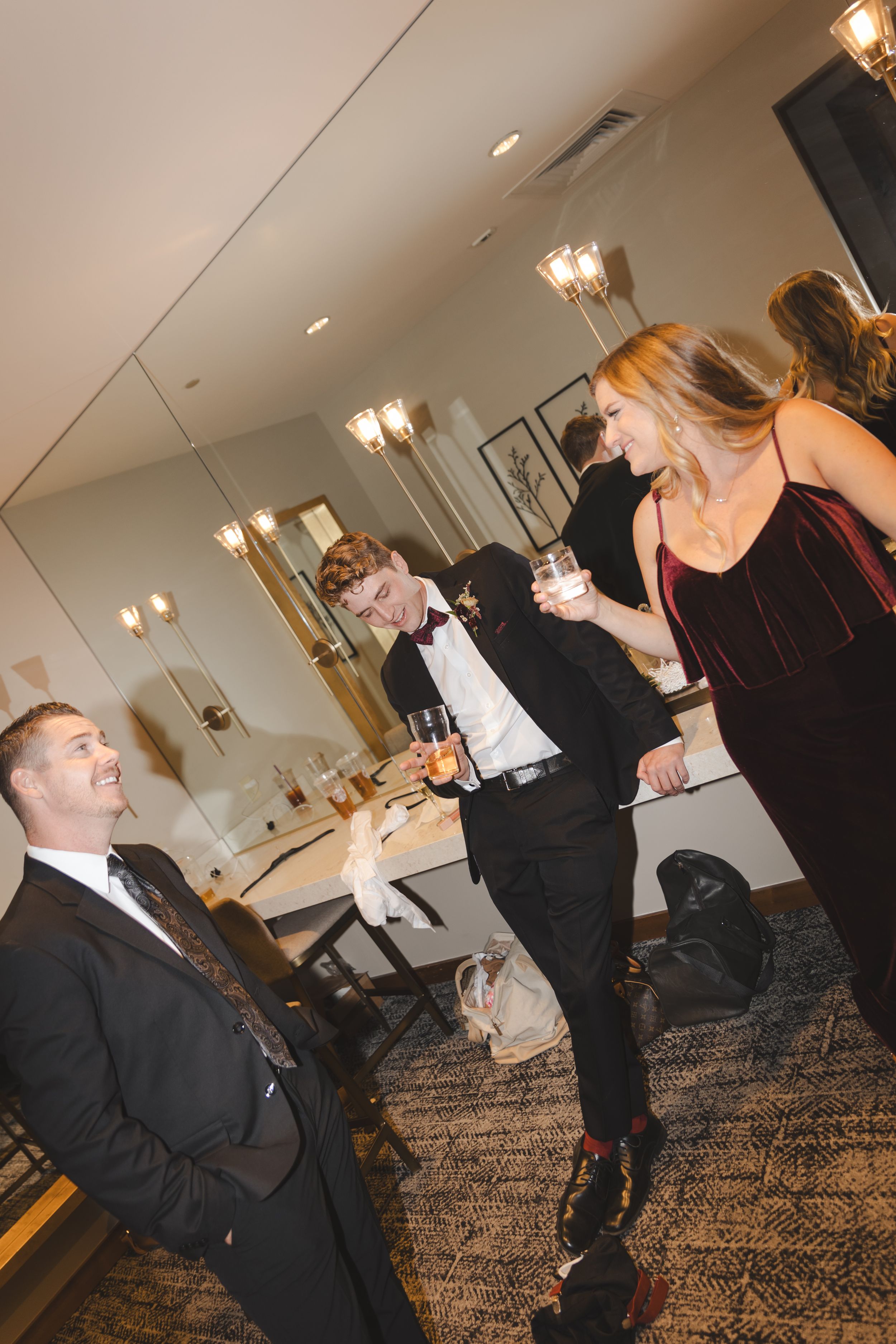 People in formal attire socializing at an indoor event with warm lighting and carpeted floors.