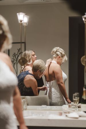 Wedding preparations showing final touches being made in an elegant dressing room with mirrors and lights.