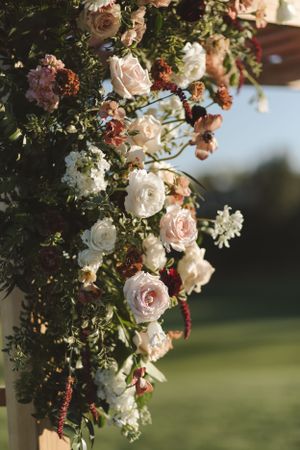 Beautiful floral wedding arch decorated with pink and white roses and greenery against a blurred outdoor background.