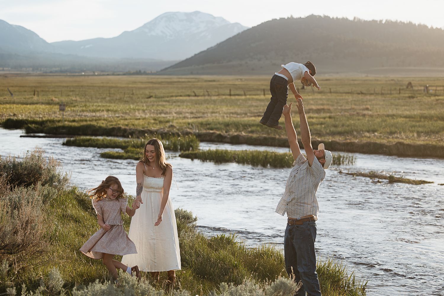 People playing and having fun near a river with mountains in the background.