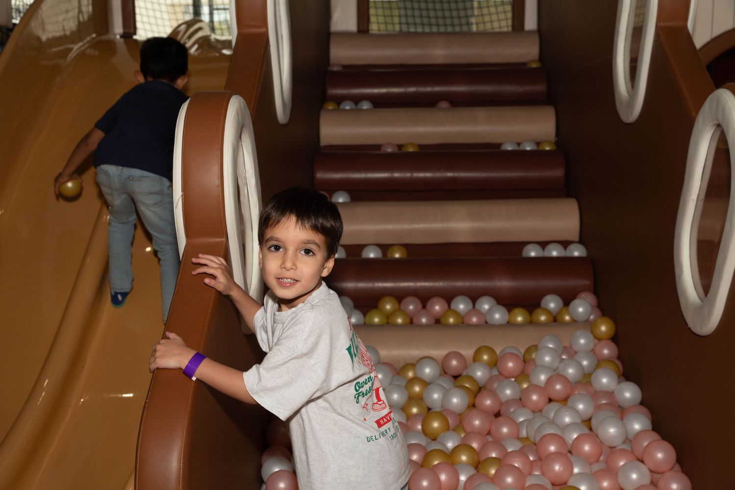 Child playing on indoor slide surrounded by colorful ball pit balls.