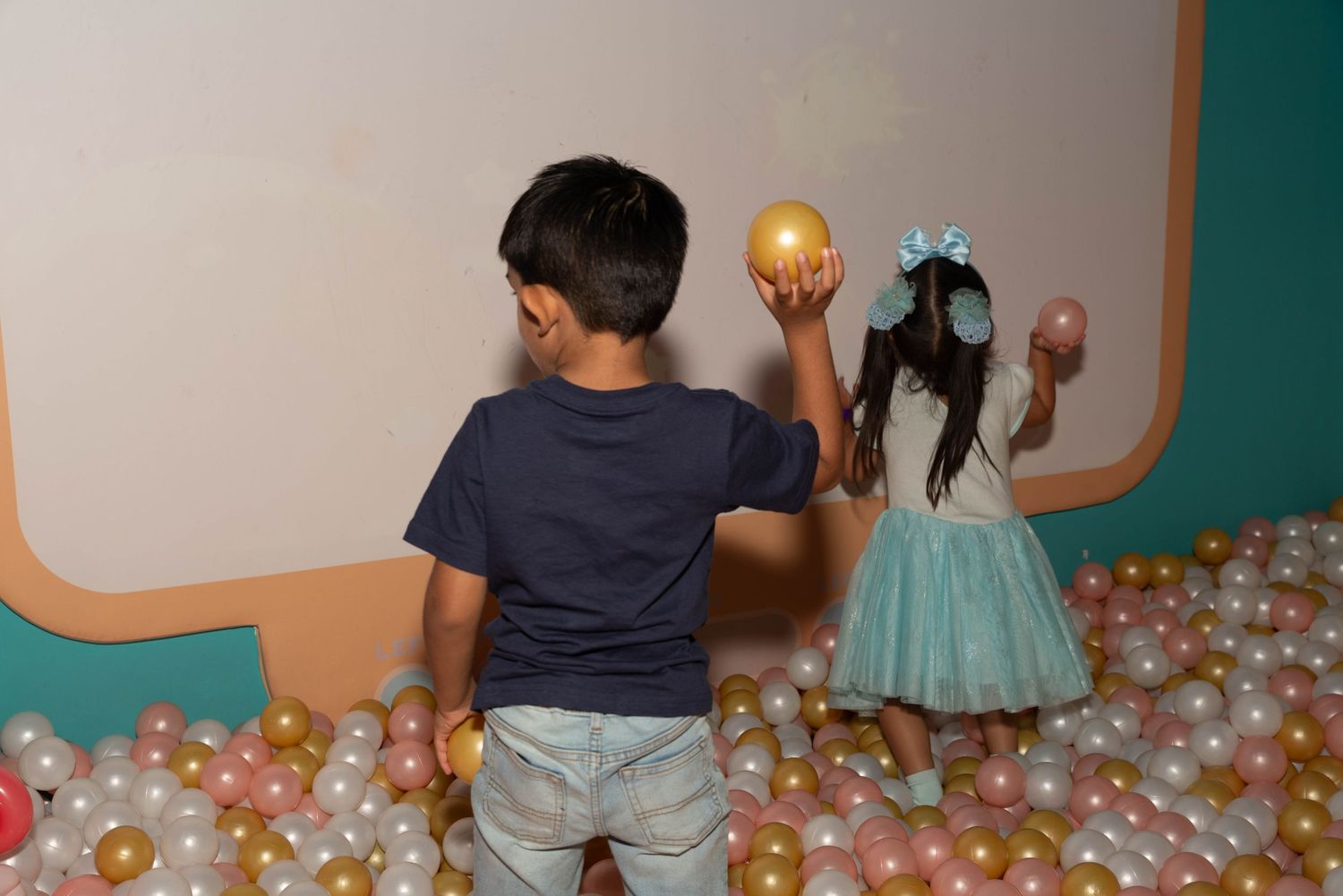Children playing with golden balls in a ball pit with decorative elements.