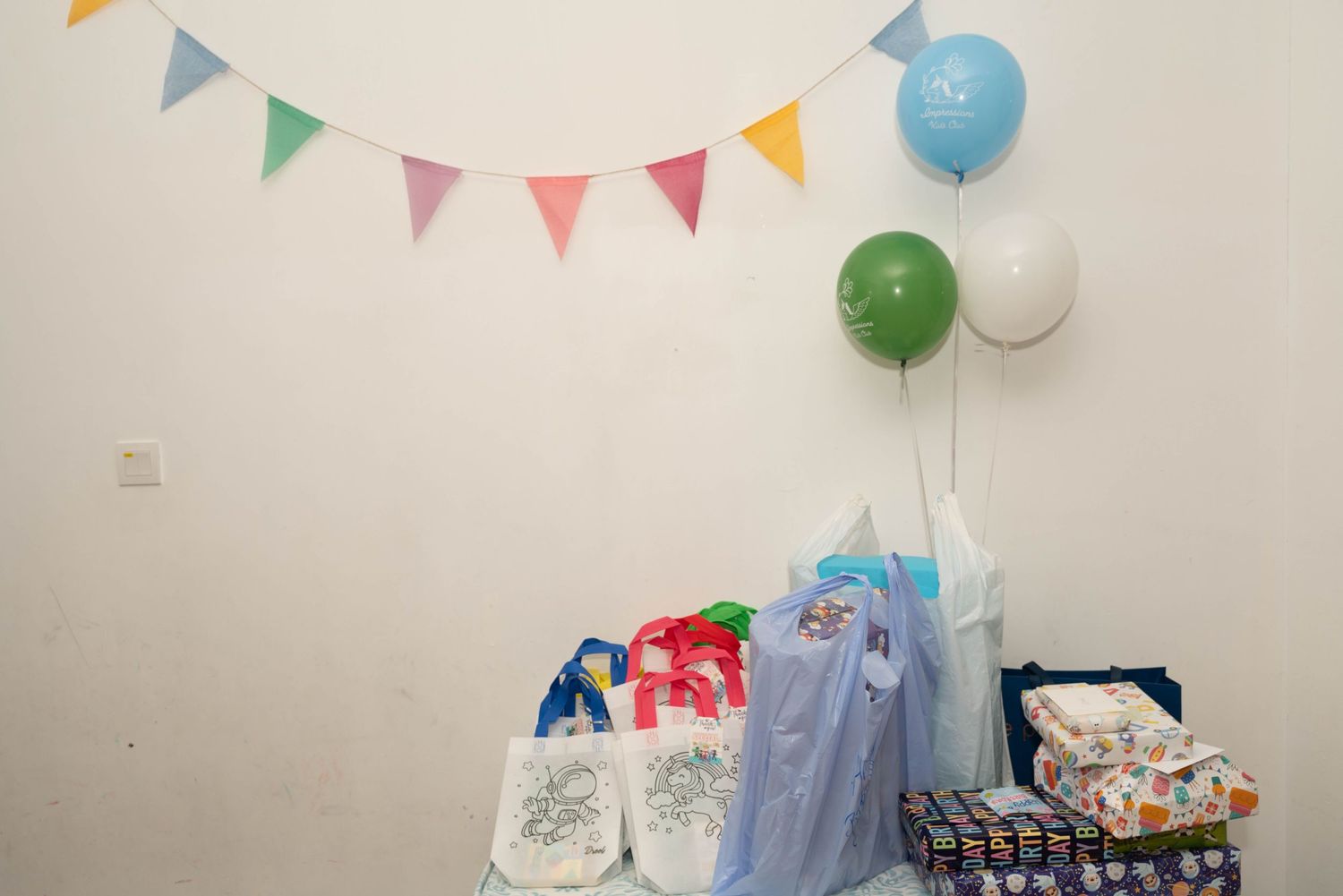 Birthday party decorations with colorful bunting flags and balloons against a white wall.