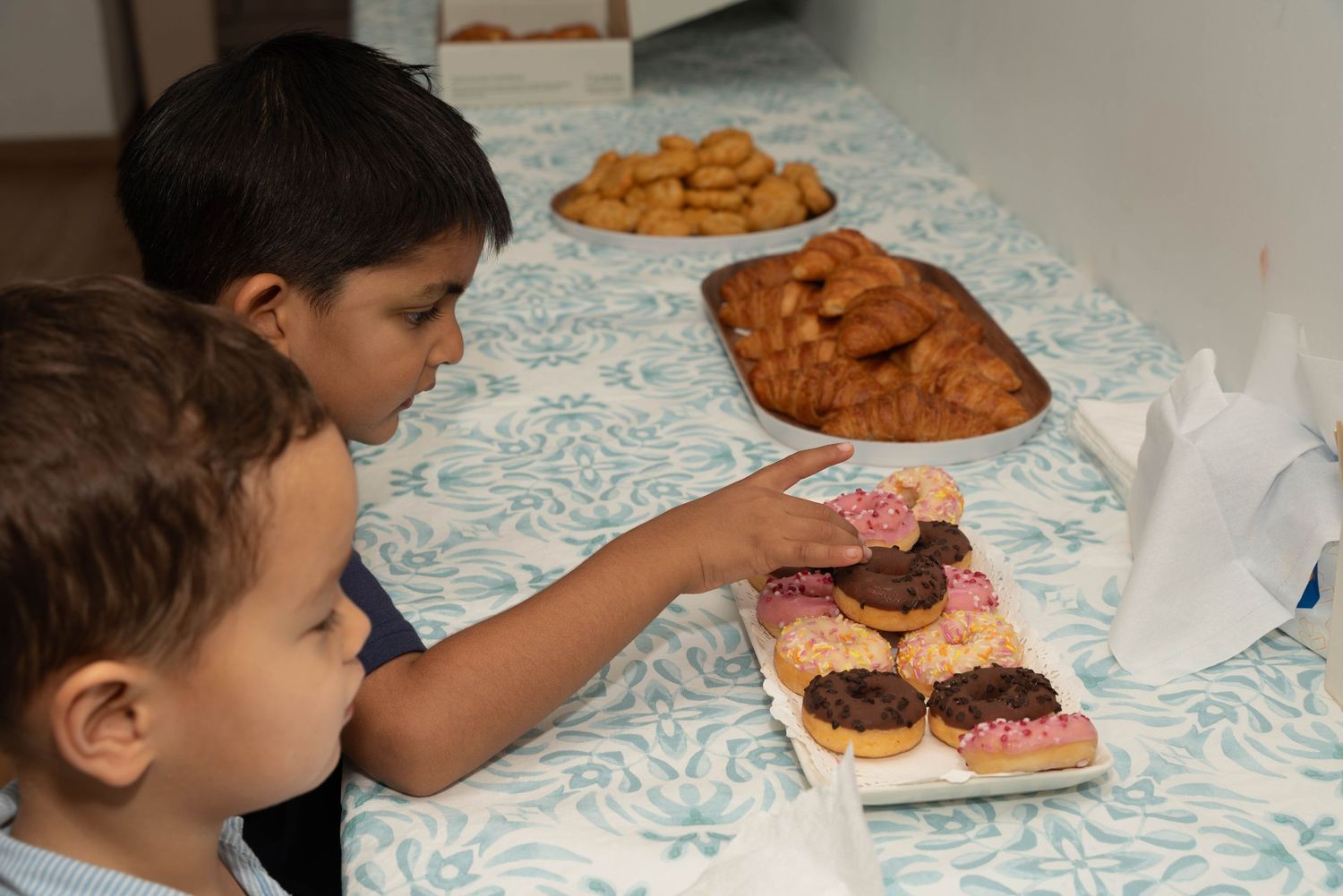 Two children reaching for desserts on a table with pastries and cookies.