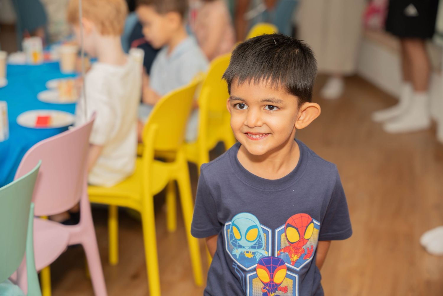 A child wearing a navy t-shirt with colorful graphic design smiles at a birthday party.
