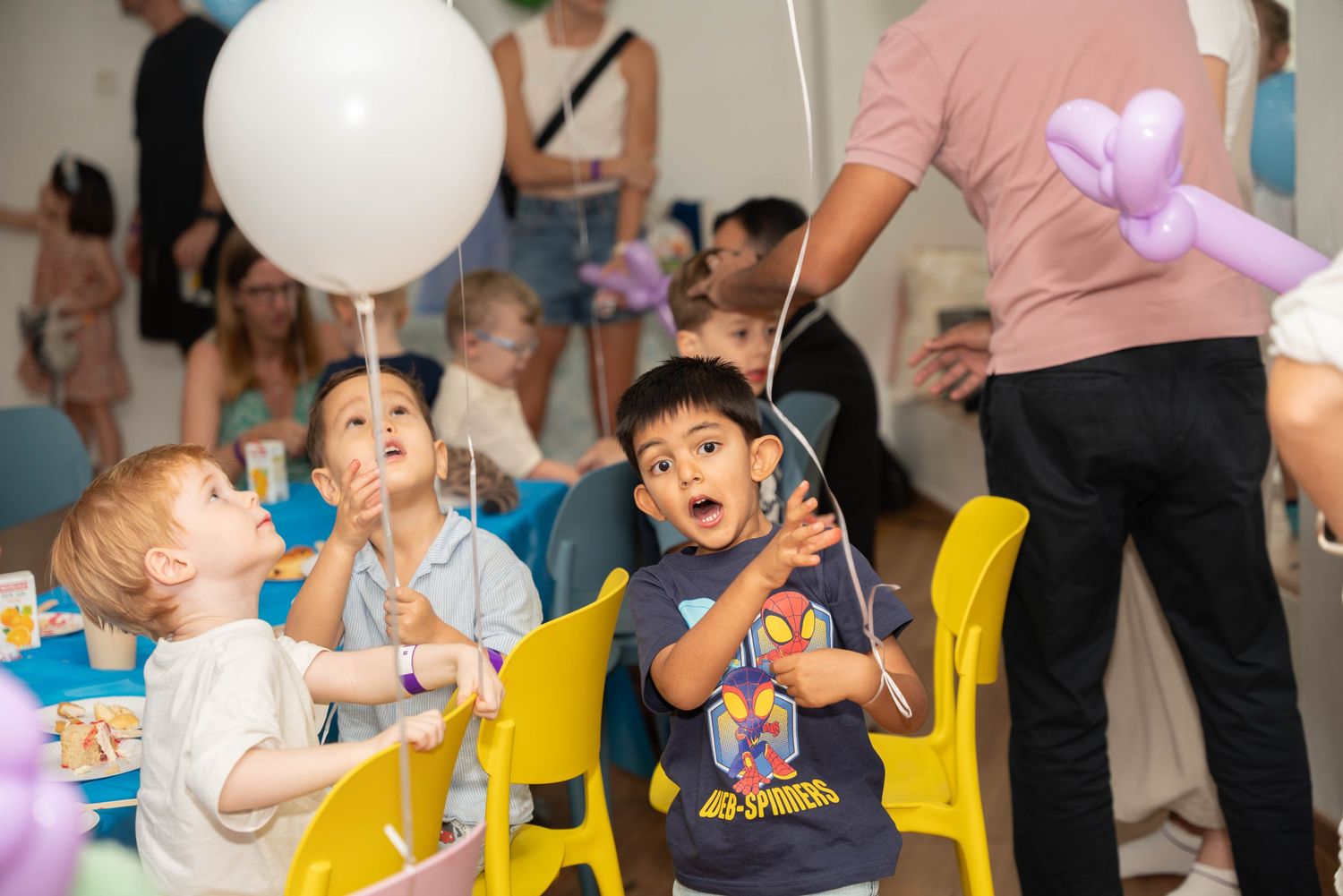 Children celebrate with white balloons and party decorations in a festive indoor setting.