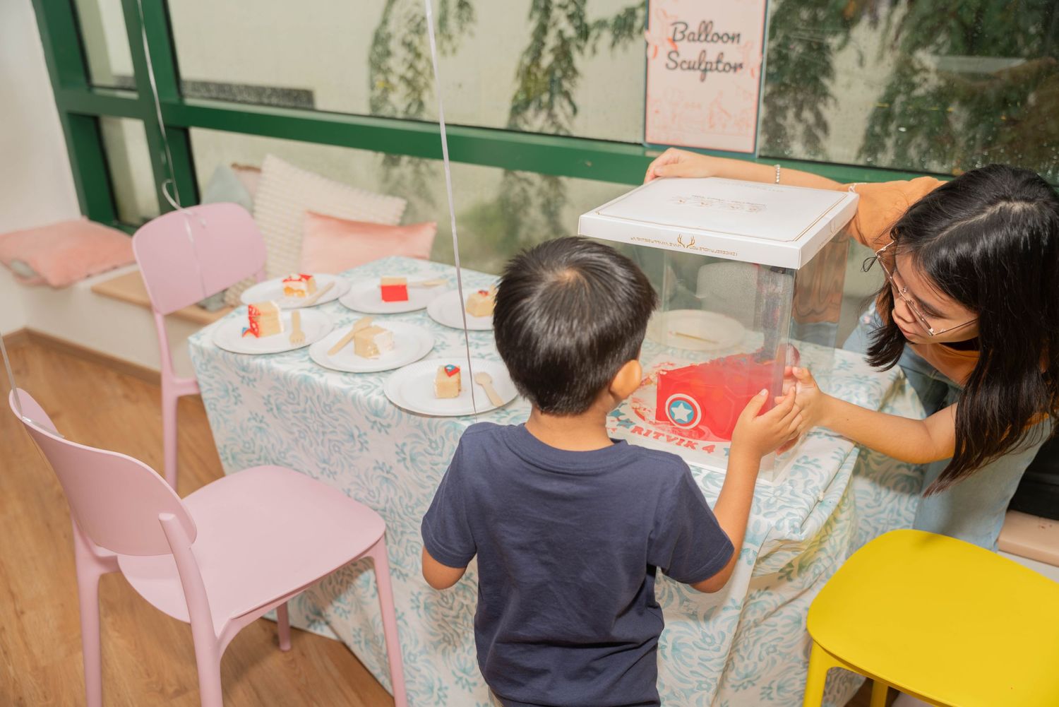 A birthday party setup with pink chairs and decorated tables in a bright room.