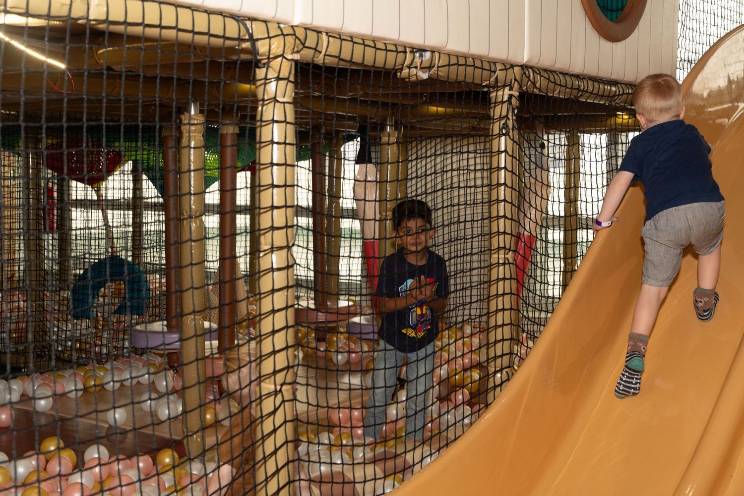 Indoor playground with mesh climbing structure and orange slide filled with play balls.