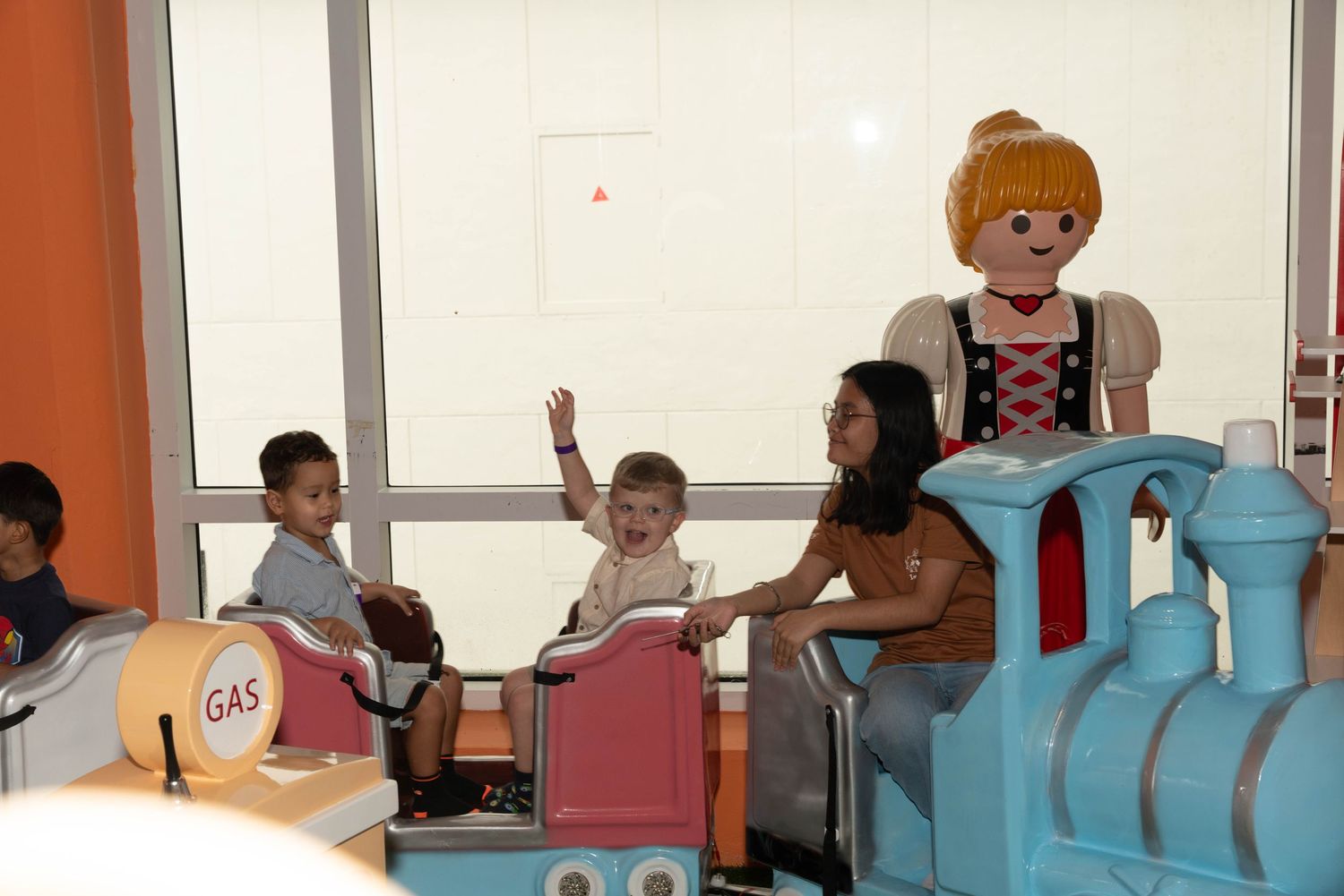 Children riding on colorful indoor train ride with costumed character.