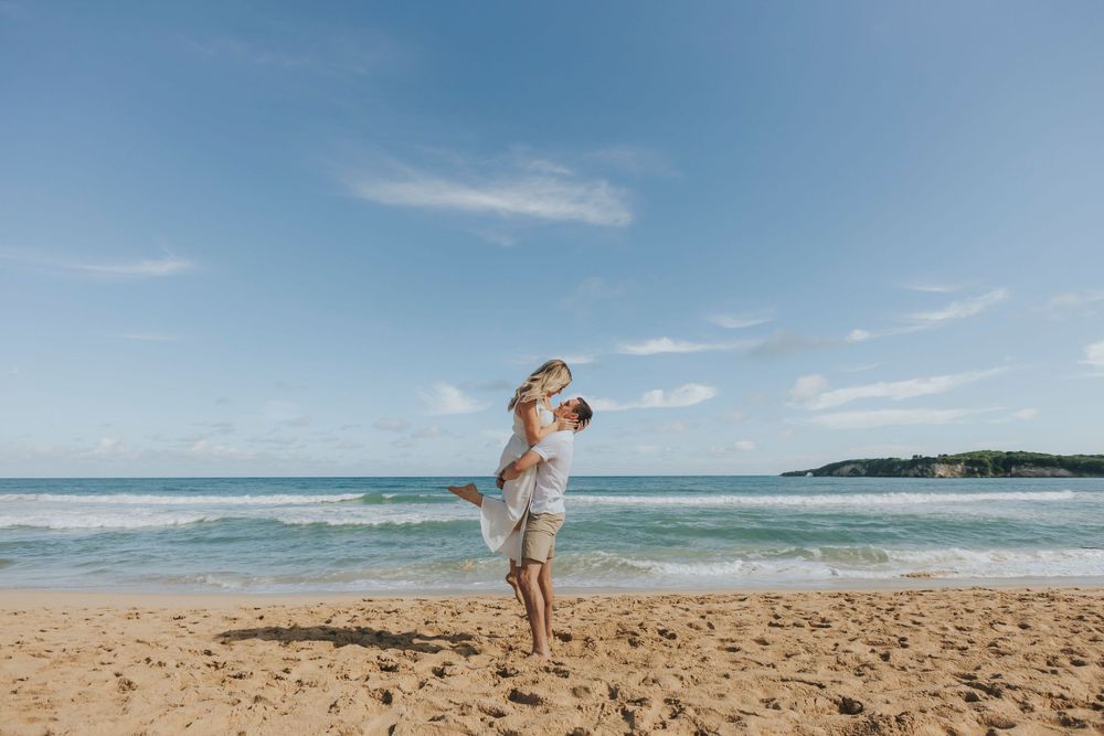 Playful couple enjoying a romantic moment on sunny beach with ocean backdrop.