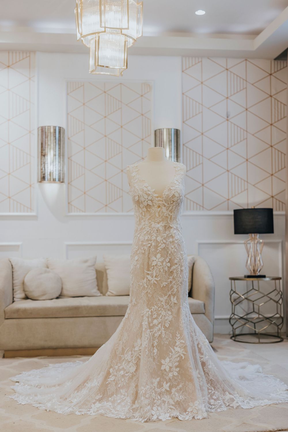 Elegant lace wedding dress displayed in luxurious bridal boutique with geometric wallpaper.