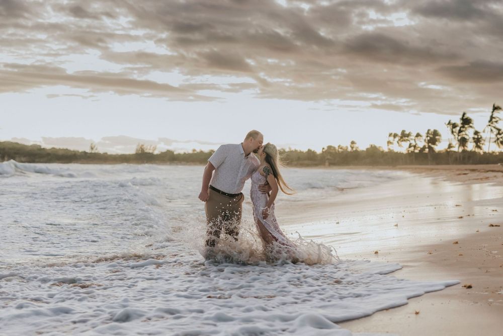 Two people splashing and walking together along a tropical beach at sunset with waves and palm trees in the background.