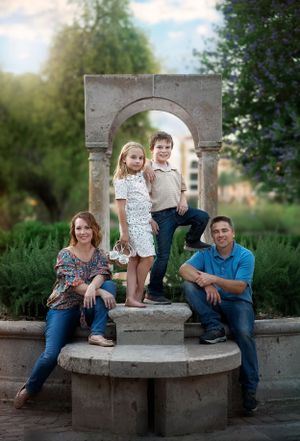 A family poses together on a stone structure with an arched backdrop in a beautiful garden setting.