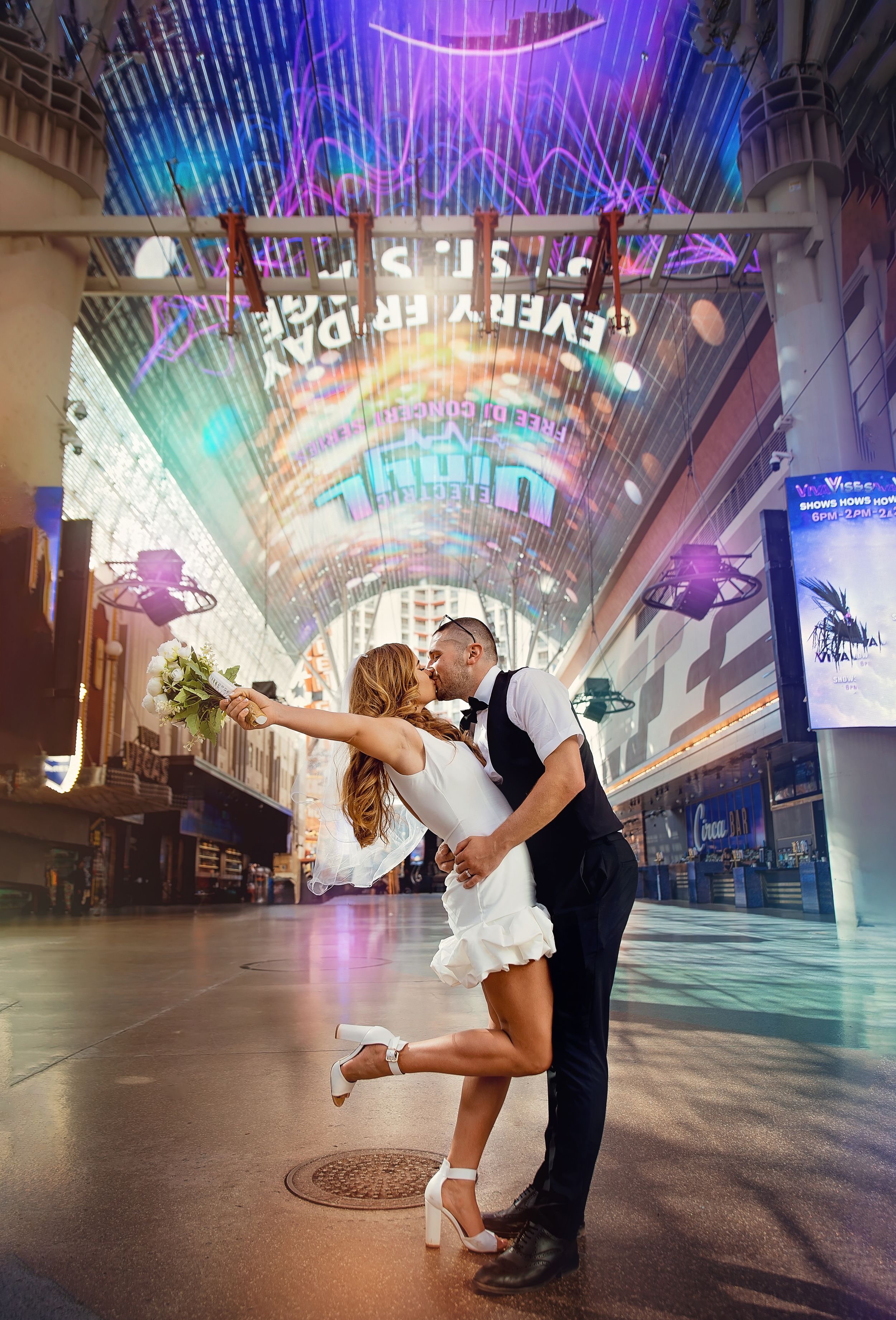 A romantic couple embraces in a dramatic dip under the neon-lit Fremont Street Experience canopy in Las Vegas.