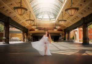 A white gown flows gracefully in an ornate architecture space with a glass ceiling and vintage light fixtures.