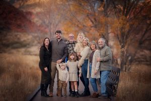 A family group poses together outdoors in autumn, wearing coordinated neutral colors against a warm fall backdrop.