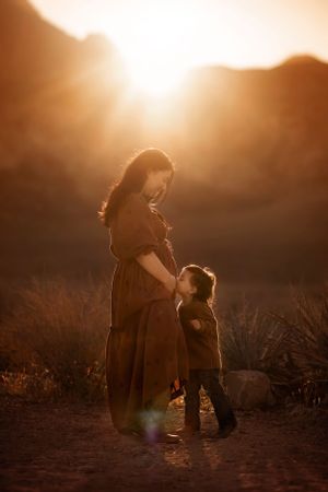 A silhouette of a mother and child standing together against a warm sunset in a desert landscape.