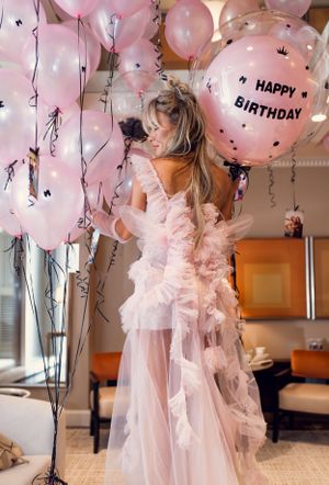 Pink and white tulle dress twirls amongst birthday balloons and streamers in a dreamy birthday celebration setting.