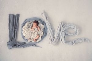 The word 'LOVE' spelled out with baby blankets and a sleeping newborn nestled in the letter O.
