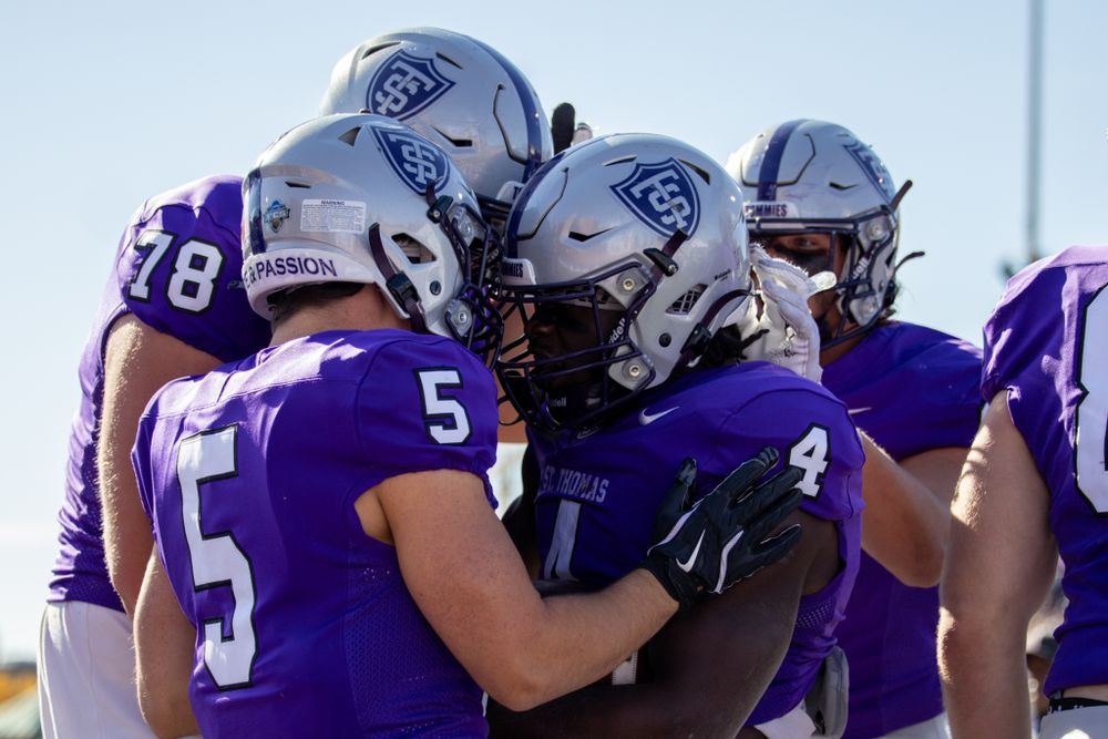 Football teammates in purple jerseys huddle together during game.