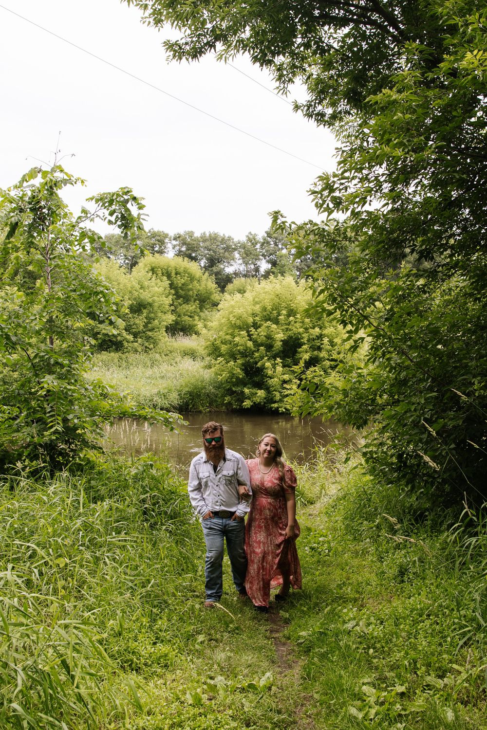 A couple walks together through a lush green meadow path on a sunny summer day.