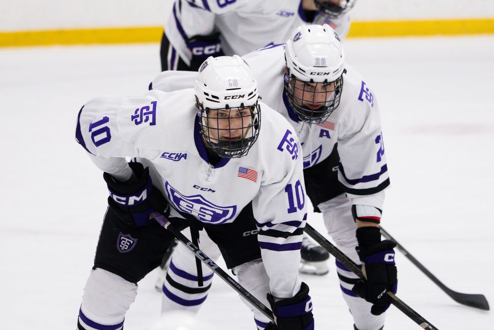 Two hockey players in white and blue uniforms skate together during a game.