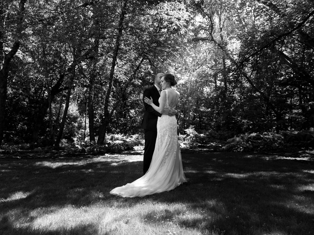 Black and white photo of a bride and groom sharing a romantic moment in a lush, tree-lined garden.