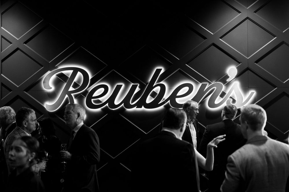 People dancing and socializing in a dimly lit nightclub with a retro-style neon sign on the wall.