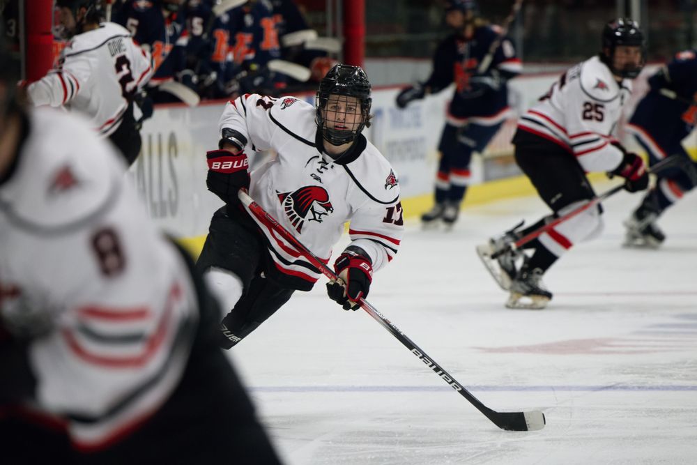 Hockey player in white jersey handles puck during intense game action.