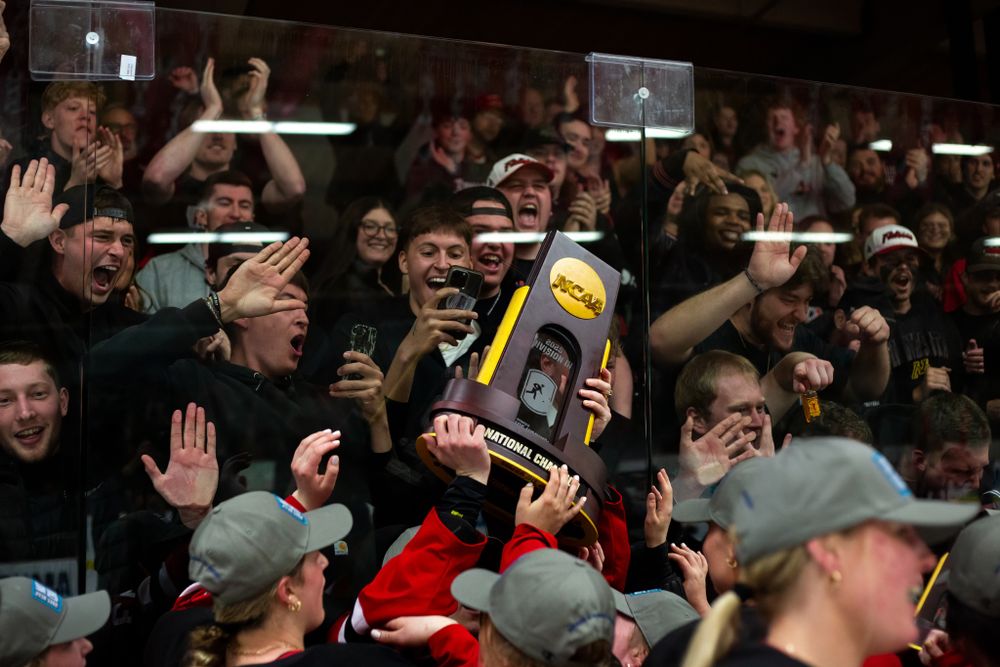 Excited fans in a crowded stadium section hold up a trophy during a sports celebration.