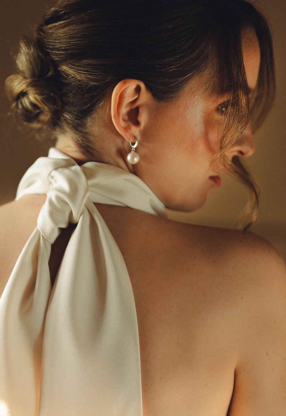 Elegant white bow detail on back of wedding dress against neutral background.