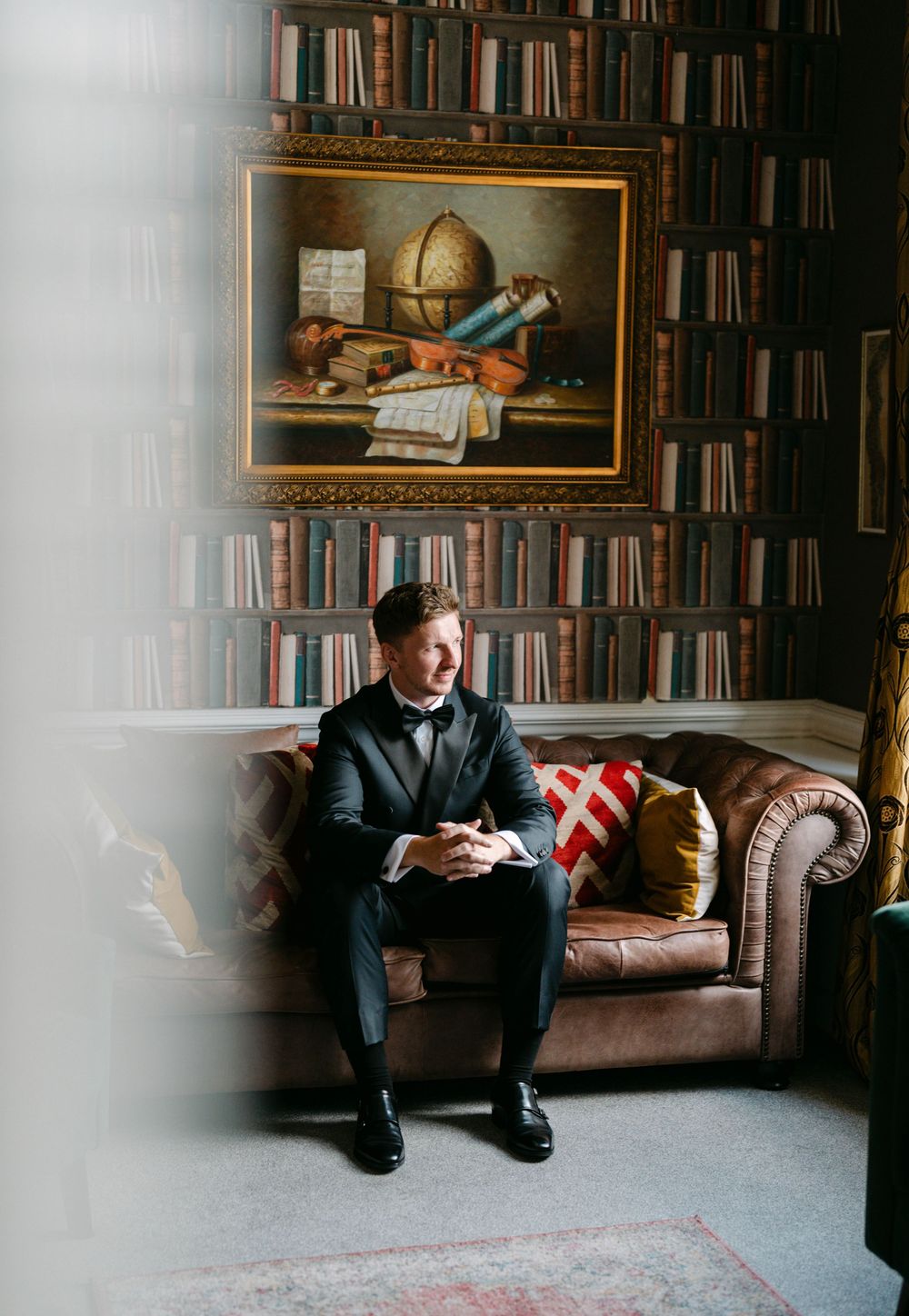 Moody portrait series in a library with leather couch and wall-to-wall bookshelves.