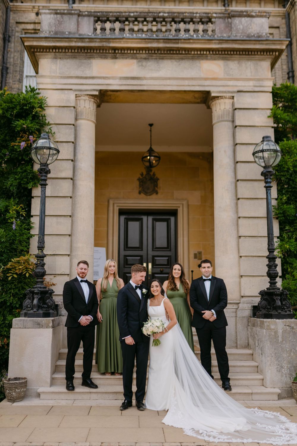Wedding party poses elegantly in front of grand stone entrance with classic architectural details.