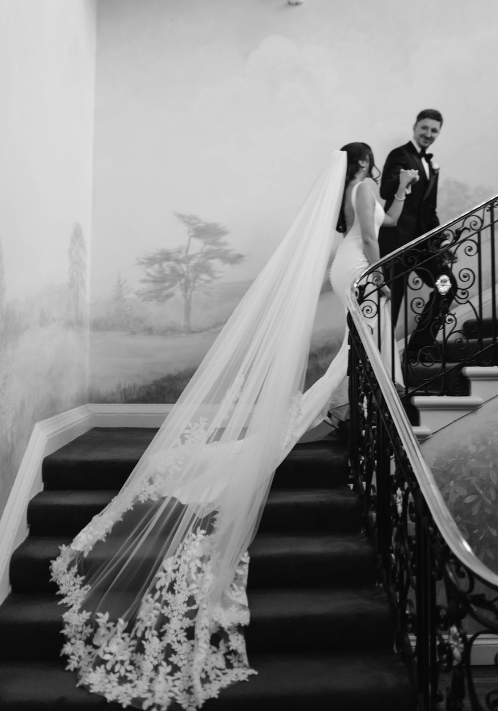 Long lace wedding veil trails dramatically down ornate staircase in black and white.