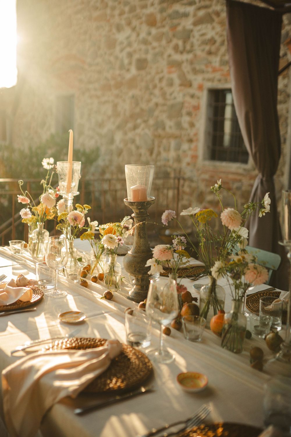 Romantic wedding reception table with candlelight and floral centerpieces against stone wall.