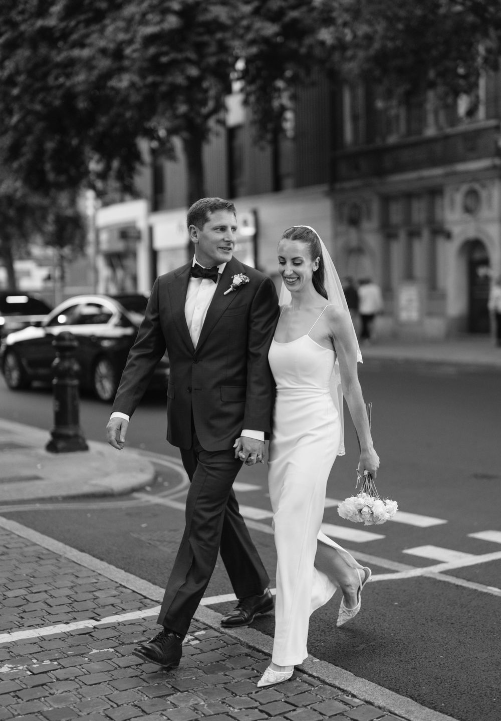 Black and white photo of a couple walking together on a city street after their wedding ceremony.
