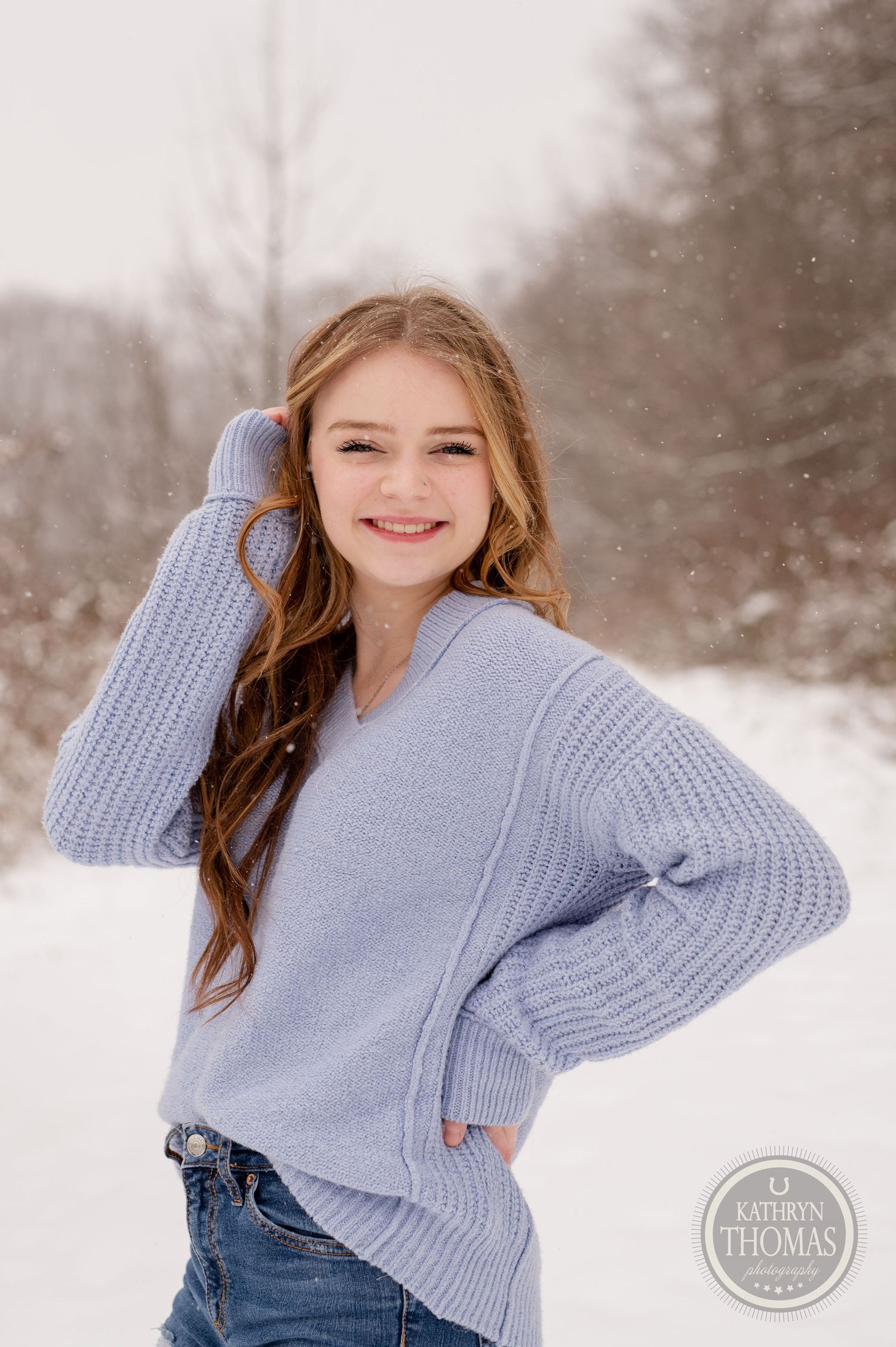 Winter portrait featuring person in cozy blue sweater against snow-covered trees.