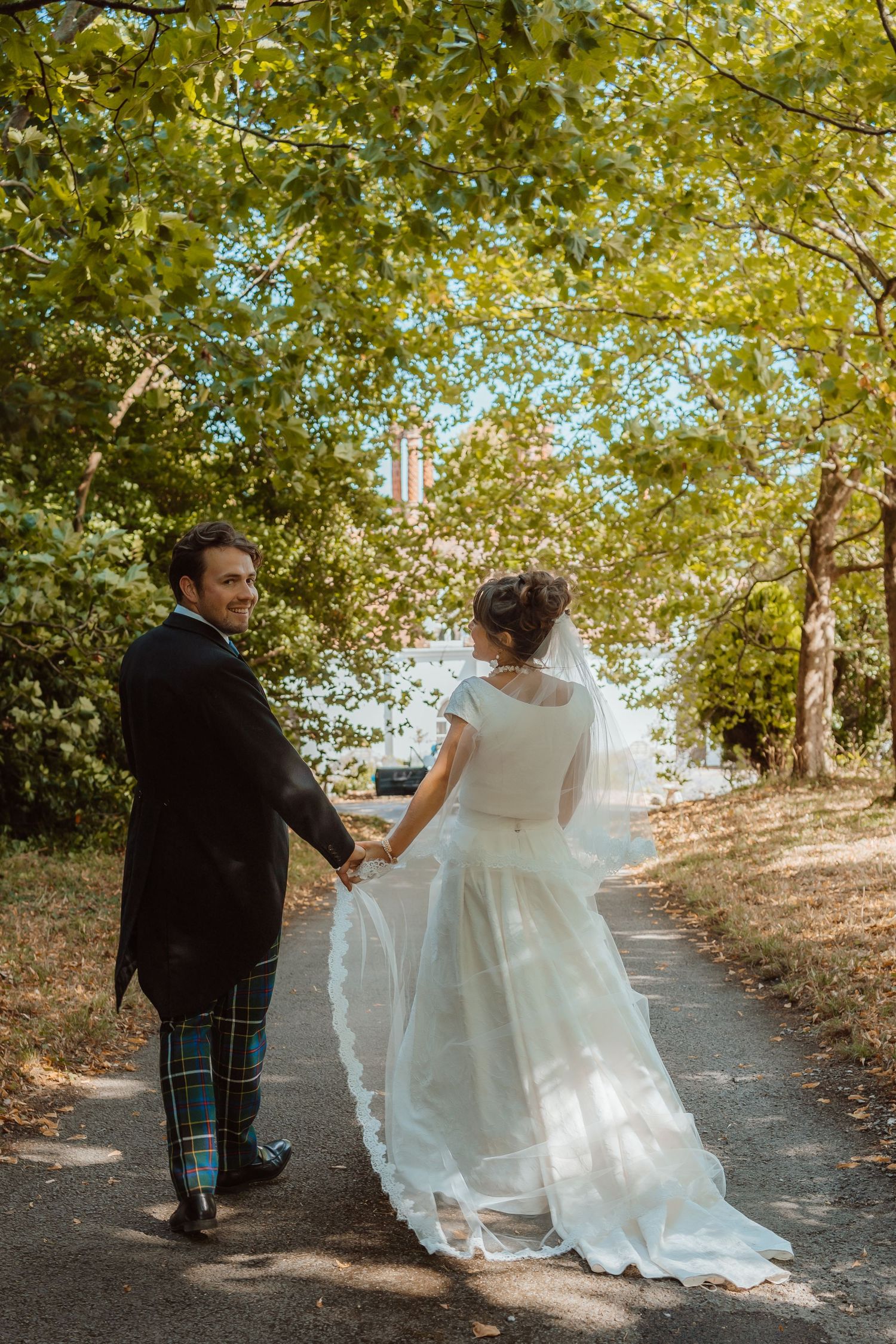 Black and white wedding portrait of couple holding hands in front of historic stone mansion.