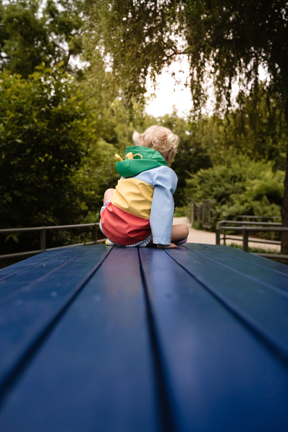 Child sits on blue fish in a bright contrasting jacket at Tulsa Gathering Place. Image captured by Tulsa Photographers Cristin Franks